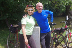 Joseph Brosky and Donna Brosky standing next to two bicycles outside with trees behind them.
